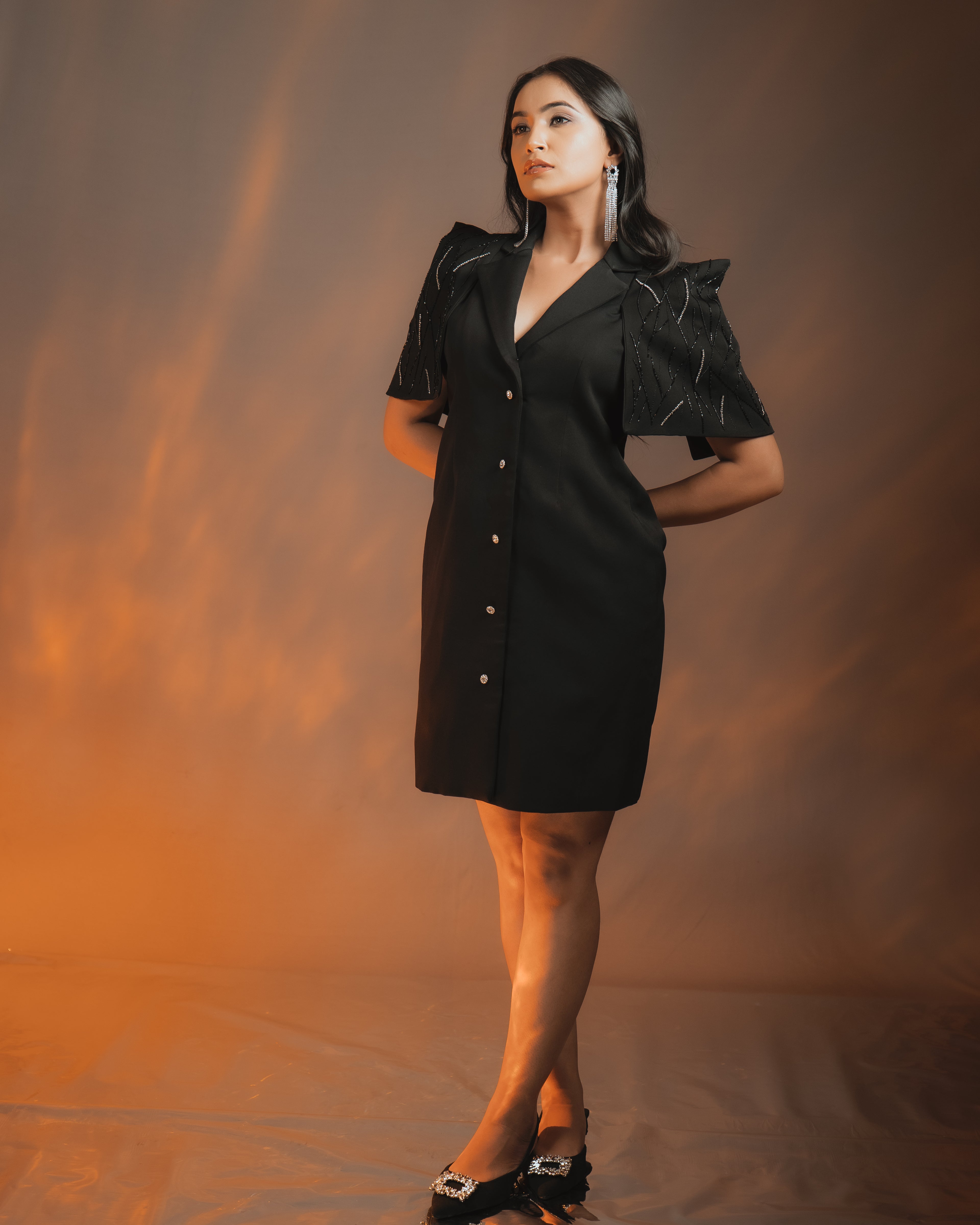 Model showcasing the ZEN BLAZER DRESS BLACK with embellished cape sleeves and a Swarovski crystal button.